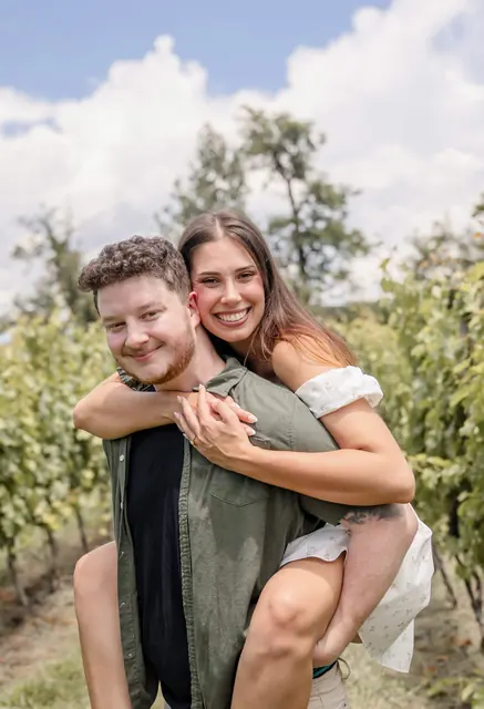 Katie riding piggyback on David's shoulders in the vineyard, both laughing