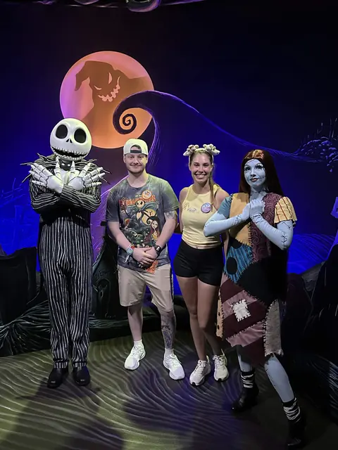 Katie and David posing with Jack Skellington and Sally beneath a grinning moon